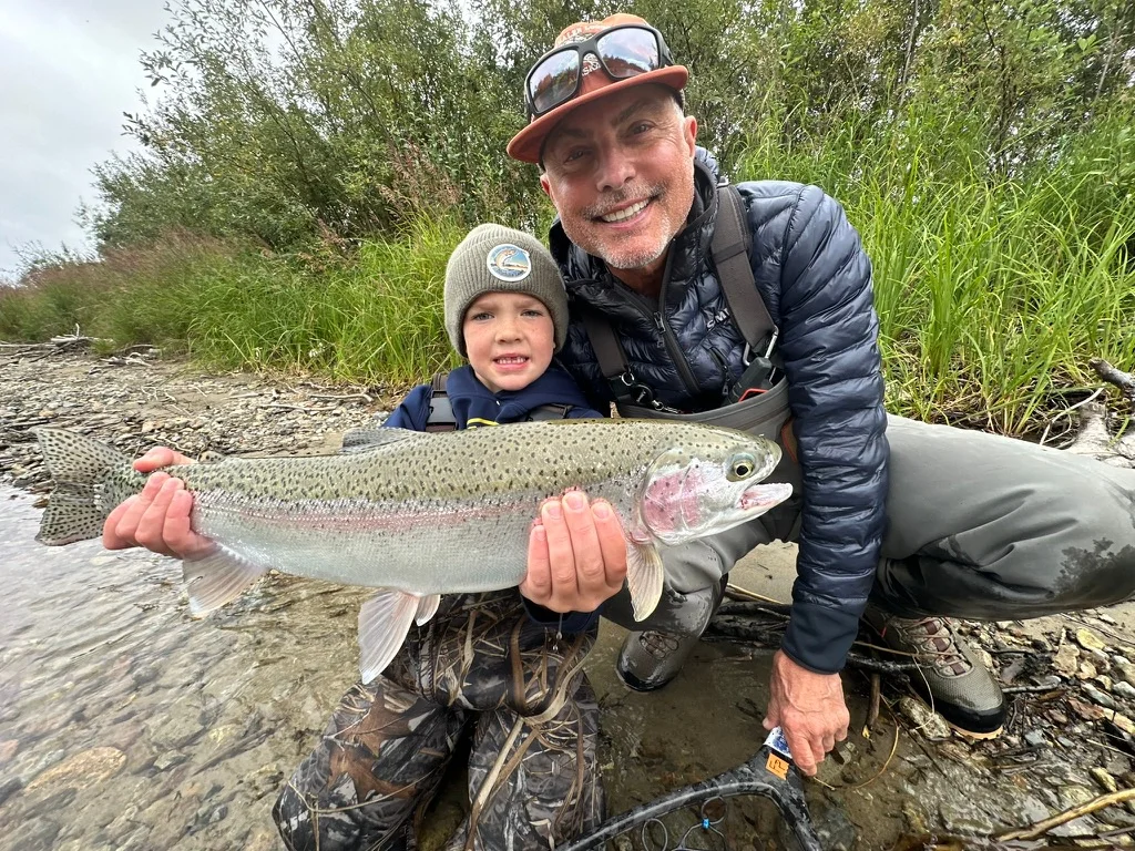 Father and son proudly holding a trophy wild Rainbow Trout on the riverbank